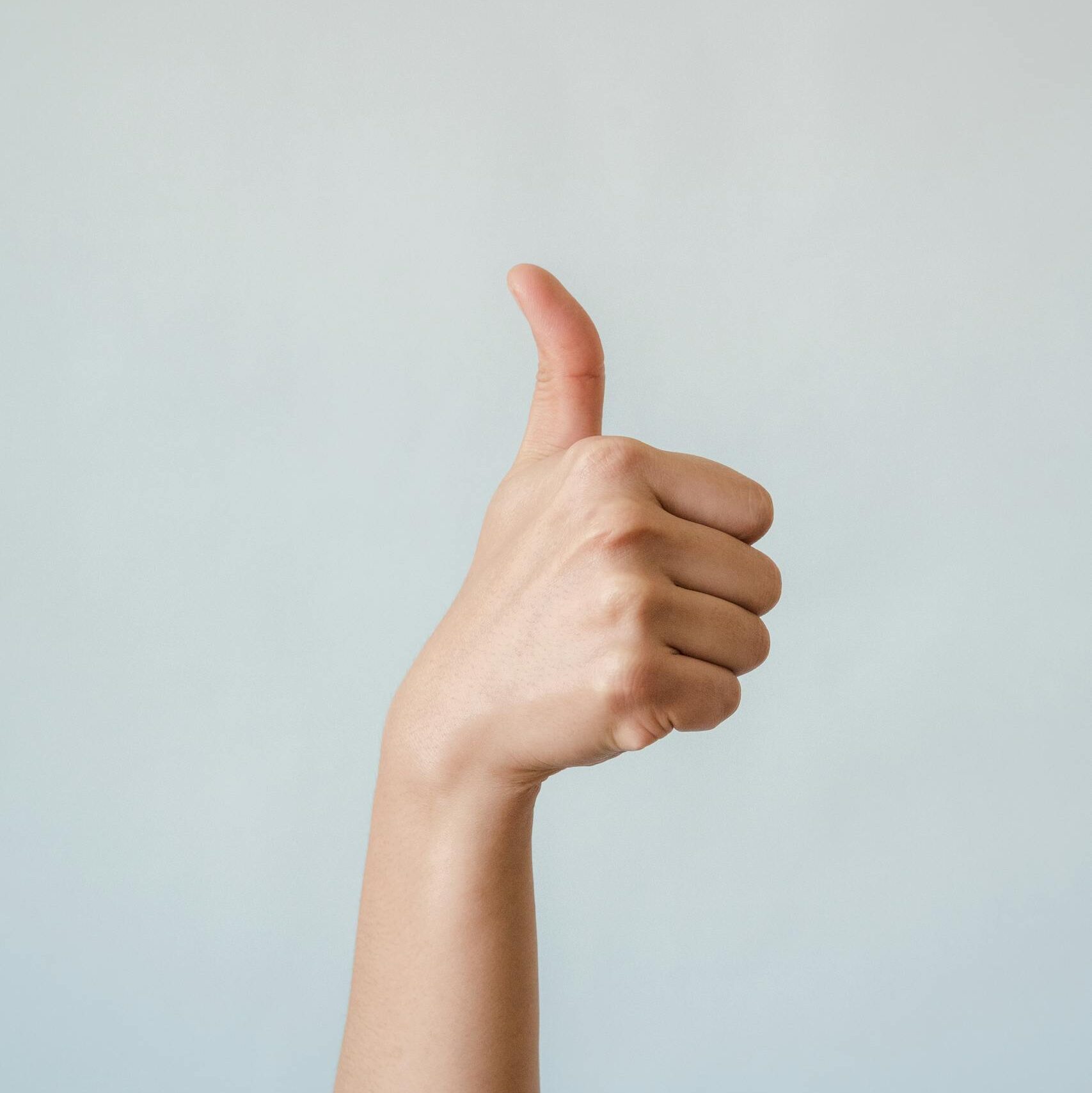 Close-up of a hand showing a thumbs up gesture on a blue background.
